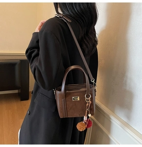 Detail of dark brown bucket bag featuring faux leather textures and plush ball charm