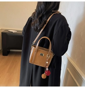 Detail of a brown suede crossbody bag with leather trim and stylish pompom charm