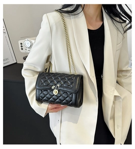 Detail of black quilted chain bag featuring a gold rabbit ear lock on a beige blazer