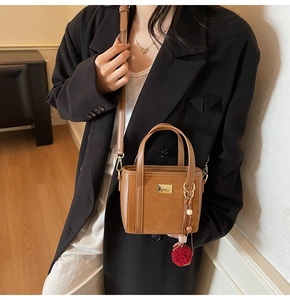 Close-up of brown bucket bag with tassel charm and adjustable shoulder strap on model