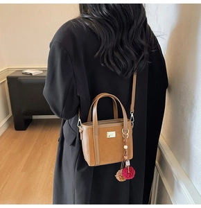 Detail view of camel suede bucket bag with dual leather handles and pom-pom charm