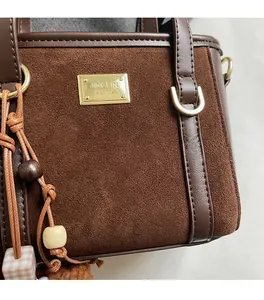 Detail of dark brown suede bucket bag with gold metal plate and beaded charm pendant