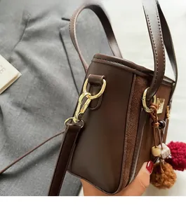 Close-up of brown leather bucket bag featuring gold hardware and plush pom-pom charms