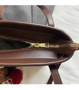 Detailed close-up of smooth gold zipper and plush charm on dark brown suede bucket bag