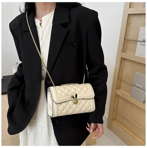 Detail of cream white quilted bag with golden rabbit ear lock and metal chain strap