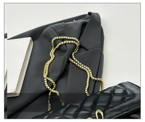Detail of black quilted shoulder bag featuring premium gold chain strap on grey blazer