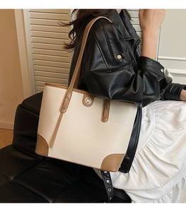 Side view of a beige and brown paneled tote bag with golden circular metal logo