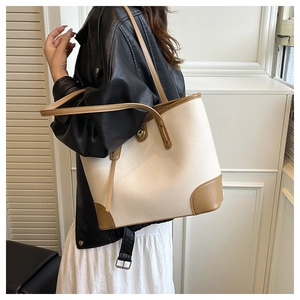Detail of minimalist cream leather tote bag with brown trim and gold clasp on shoulder