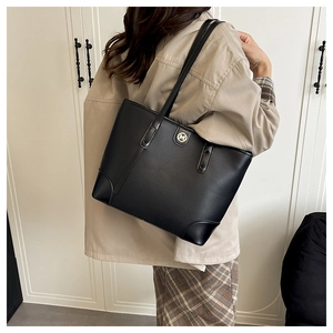 Detail of black textured leather tote bag featuring a round golden M logo on the front