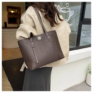Close-up of brown textured leather tote bag with metallic M logo in outdoor street setting