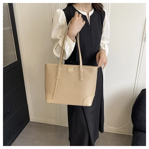 Detailed close-up of a beige faux leather tote bag with gold M logo and reinforced corners