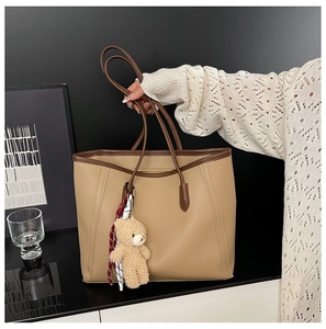 Detail of khaki lychee grain tote bag with plush bear charm and contrast dark handles
