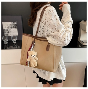 Detail of khaki tote bag with litchi texture and cute teddy bear charm on shoulder