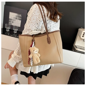 Detail of khaki faux leather tote bag with bear charm and scarf on a model