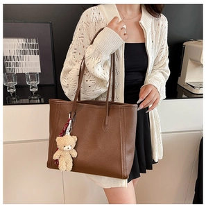 Detail of brown litchi pattern leather tote bag with a cute plush bear charm