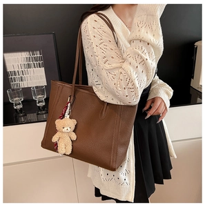 Detail of dark brown pebble leather tote bag with a cute plush bear charm on strap