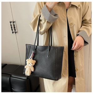 Close-up of black lychee grain leather tote bag with a cute plush bear pendant