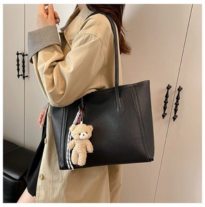 Detail of black pebble leather tote bag with shoulder straps and plush bear charm
