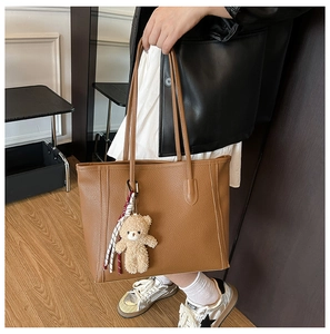 Detail of caramel lychee grain leather tote bag with plush bear and ribbon accessory