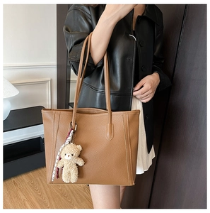 Detail of vintage brown leather tote bag with plush bear charm and printed ribbon