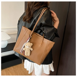 Brown leather tote bag detail with plush bear charm and ribbon on model's shoulder