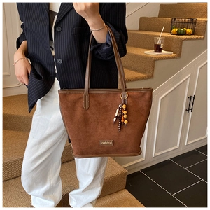 Détail d'un sac cabas en daim avec un gland en perles colorées et une plaque logo en métal