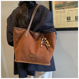 Détail du sac cabas en daim marron avec breloque en perles de bois et bandoulière en cuir