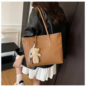 Detail of caramel brown litchi grain tote bag featuring plush bear and striped scarf