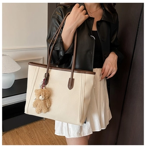 Detail of cream tote bag with brown trim and cute plush bear charm for daily commute