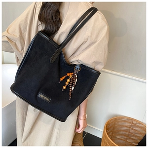 Détail d'un grand sac cabas en daim noir avec pendentif perlé et plaque de marque