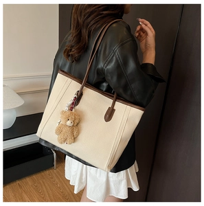 Detail of off-white faux leather tote bag with brown handles and plush bear charm decoration