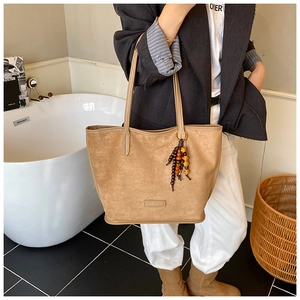 Détail du sac cabas en daim kaki avec pompon en perles de bois et logo en cuir élégant