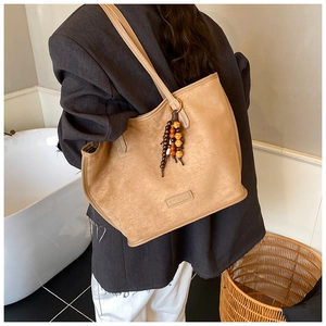 Détail du cabas en daim avec pompon en perles et plaque logo sur texture douce