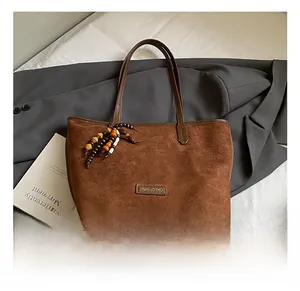 Gros plan d'un sac cabas en daim marron avec logo métallique et pompon en perles