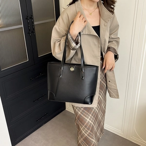 Minimalist black leather tote bag with gold M logo on a model in a modern room