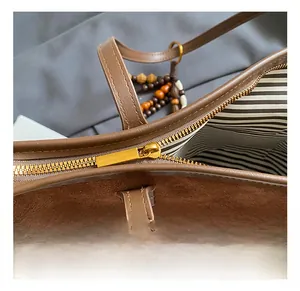 Détail du sac à bandoulière en daim avec zip doré et doublure intérieure rayée