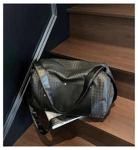 Detail of black woven texture Boston travel bag on dark wooden stairs with leather straps