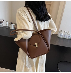 Dettaglio di borsa tote marrone scuro con fibbia dorata e tracolla in pelle sul modello