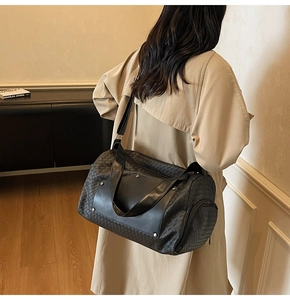 Detail of black woven travel bag featuring leather texture and adjustable shoulder strap