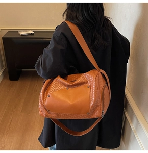 Close-up of orange woven hobo bag featuring leather patches and vintage rivets detail