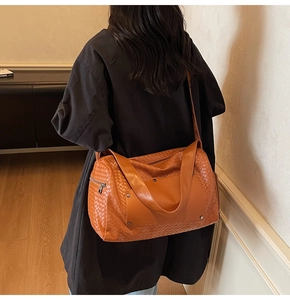 Rear view of model carrying a large orange woven leather tote bag with wide straps