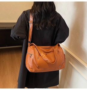 Brown woven texture travel bag shown worn as a shoulder bag on model with adjustable strap