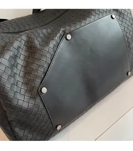 Detail of woven black leather duffel bag featuring silver rivets and zipper closure