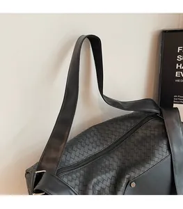 Detail of wide shoulder strap and woven checkerboard leather texture on black travel bag