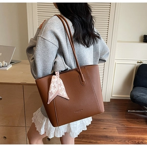 Détail du sac cabas en cuir marron grainé avec élégant foulard pied-de-poule sur la poignée