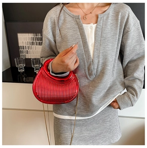Detail of red metallic crescent bag with vertical stripes and fine gold chain strap