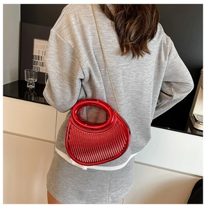 Detail of red crescent metal clutch bag featuring vertical textured lines and gold chain