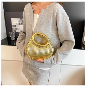 Metallic gold pleated evening bag with circular handle and chain strap on a model