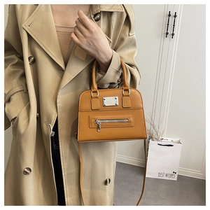 Detail of caramel leather handbag with zipper accent styled with a classic beige trench coat
