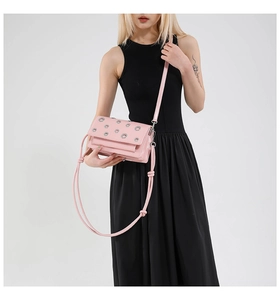 Detail of pink faux leather crossbody bag with silver eyelets and shoulder strap